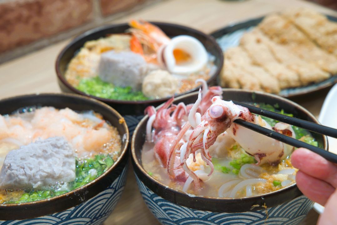 筷子正從碗中夾起一隻小卷，桌上放著多碗台式海鮮羹湯。