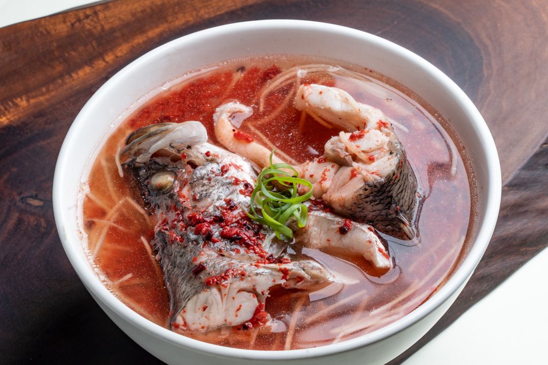 一碗紅麴魚頭湯,湯中可見大塊魚肉與麵線,灑上蔥花。