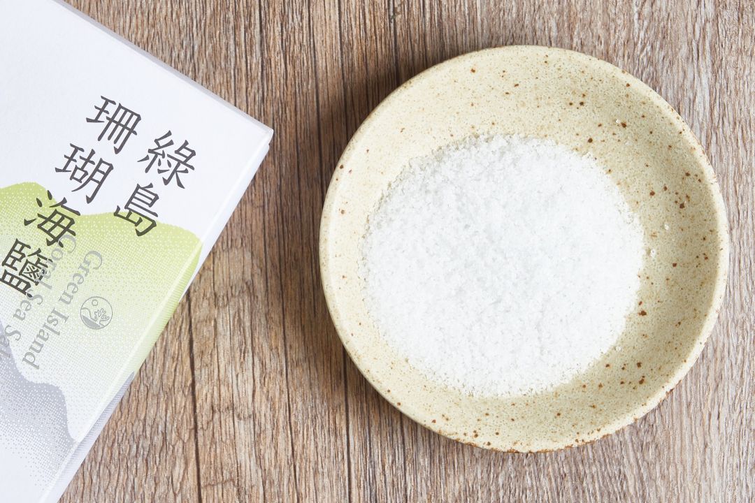 綠島珊瑚海鹽產品包裝盒,旁邊的米色陶盤上盛裝著白色海鹽顆粒。