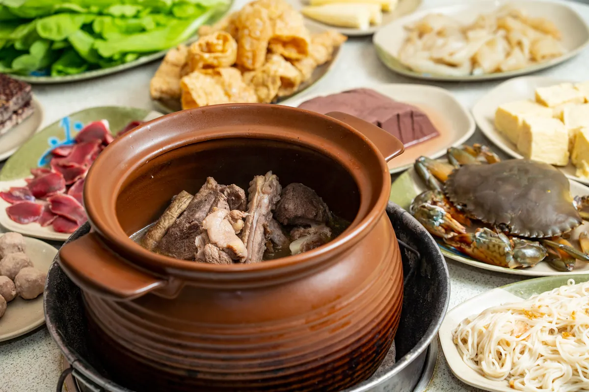特寫裝在傳統陶鍋中的台灣進補美食薑母鴨,湯頭濃郁,搭配螃蟹、紅麵線、豆皮與時蔬等豐富配料,展現獨特的海陸風味饗宴