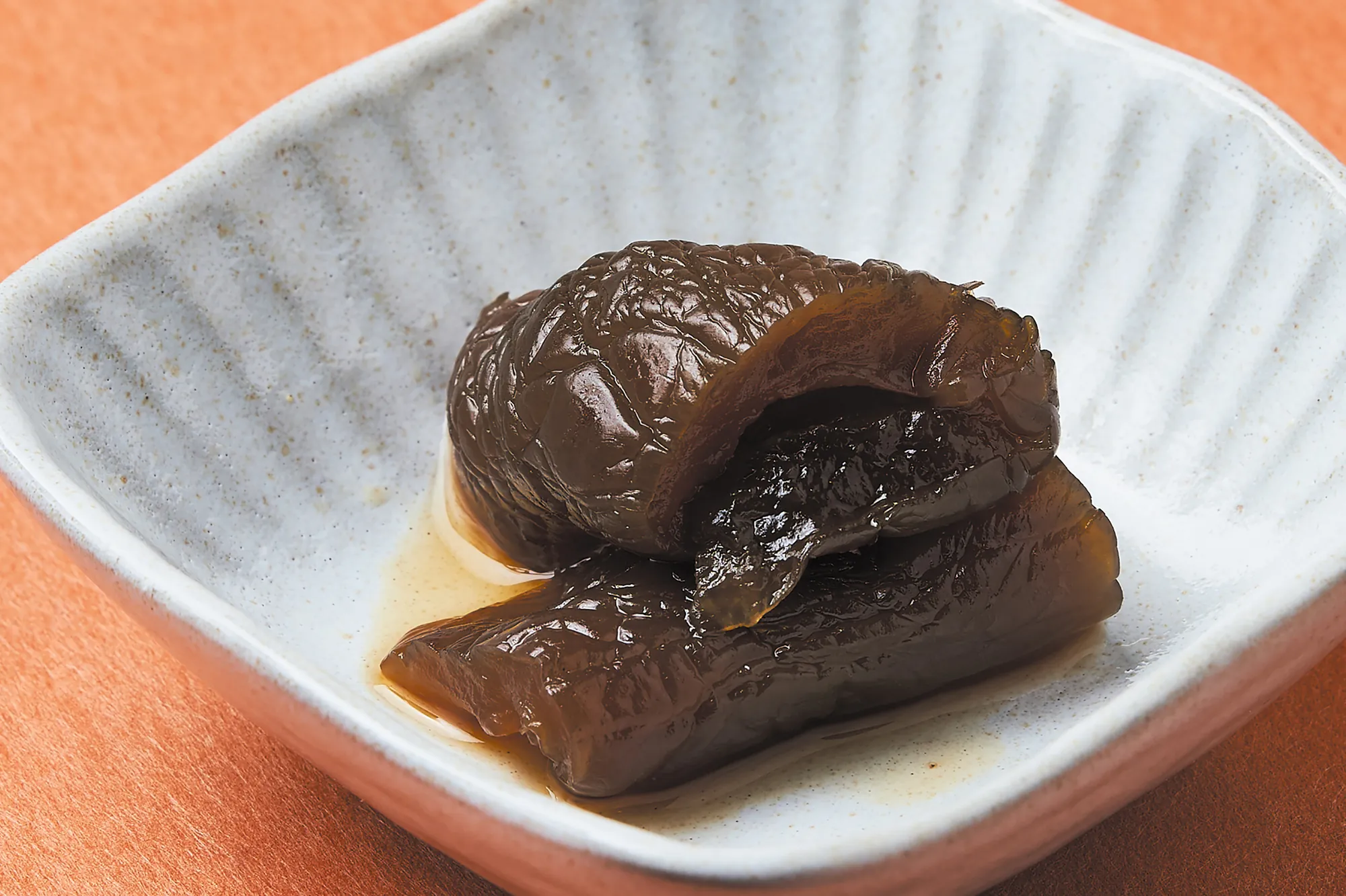 照片中深褐色的醬瓜盛裝在日式或傳統風格的淺碟中，表皮呈現醃漬後的皺縮感（這是入味與脆度的象徵），醬汁光澤誘人