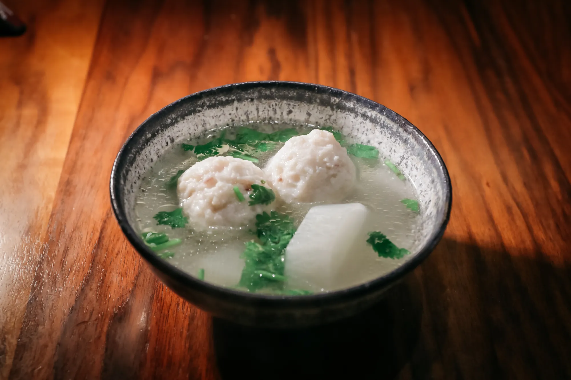 一碗清爽的台灣傳統花枝丸蘿蔔湯，碩大飽滿的花枝丸搭配鮮甜白蘿蔔塊與香菜，盛裝於日式陶碗中。