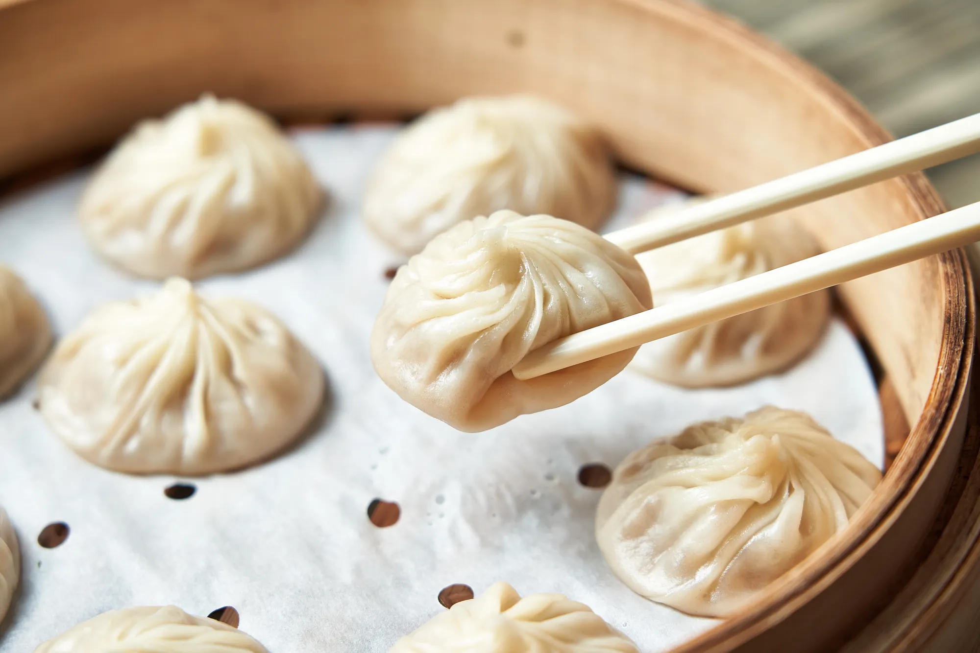 特寫鏡頭展示筷子夾起剛出爐的手工小籠包，薄透的外皮包裹著飽滿湯汁，在傳統竹蒸籠中呈現經典的台灣美食工藝