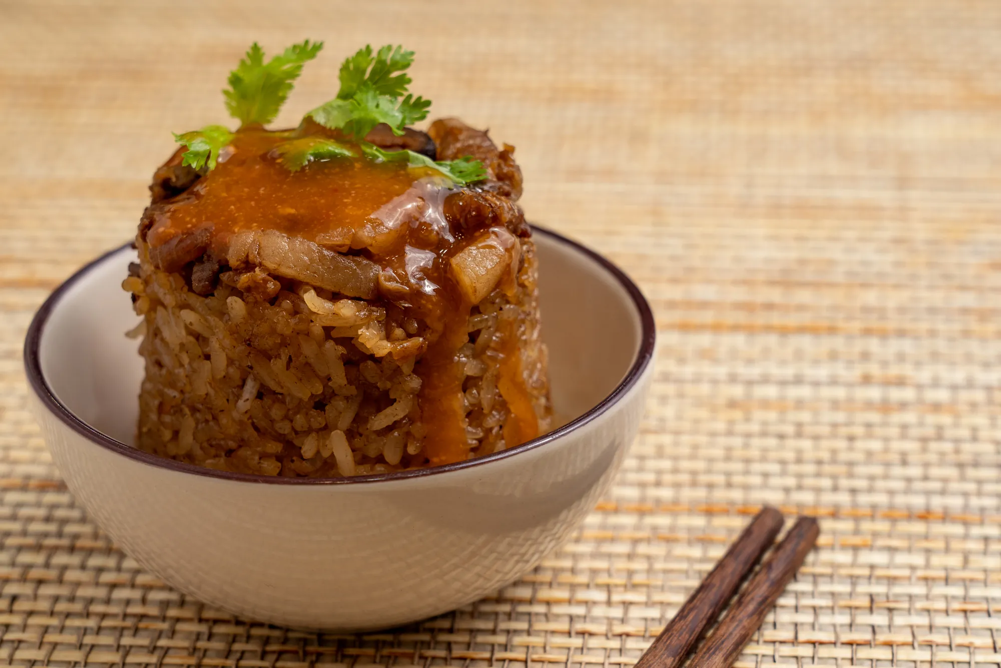 側面特寫台灣傳統小吃筒仔米糕，呈現蒸煮成型的圓柱狀糯米飯，頂端鋪滿肉燥並淋上特製醬料，口感軟糯入味。