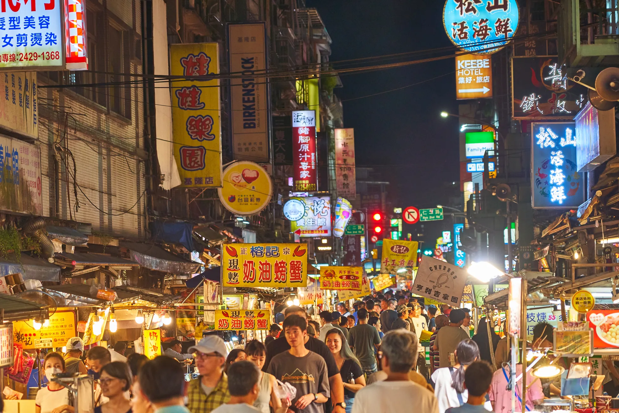 基隆夜市熱鬧的街道夜景，霓虹招牌林立，主打奶油螃蟹與現撈活海鮮料理，展現港都夜市獨有的生猛海鮮飲食文化。
