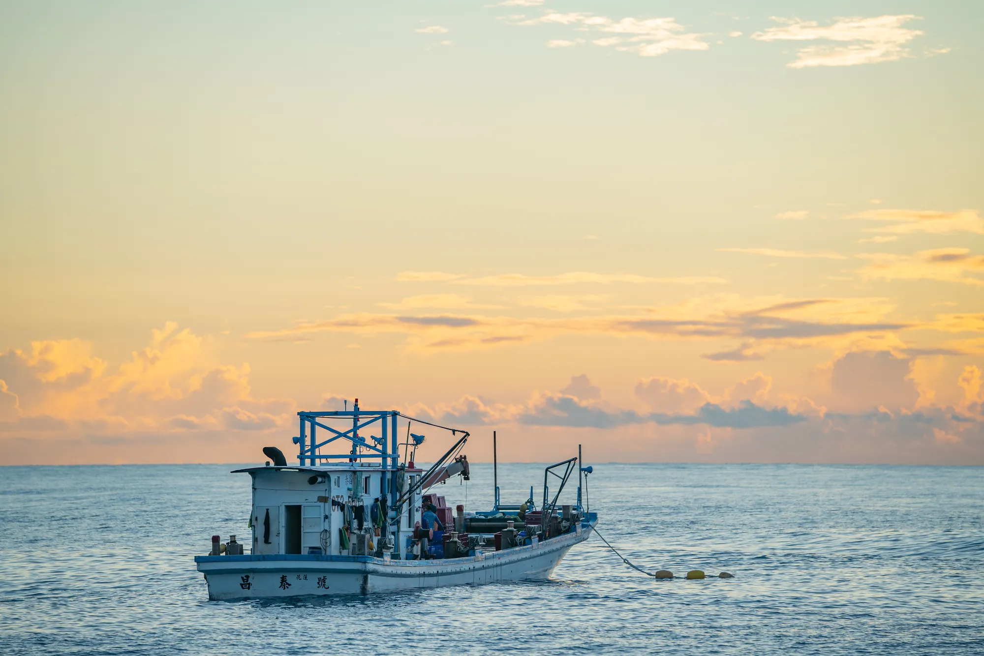 台灣小型漁船「昌泰號」在金黃色的晨曦海面上作業，象徵與海洋共存的傳統沿近海漁業與永續捕撈精神。