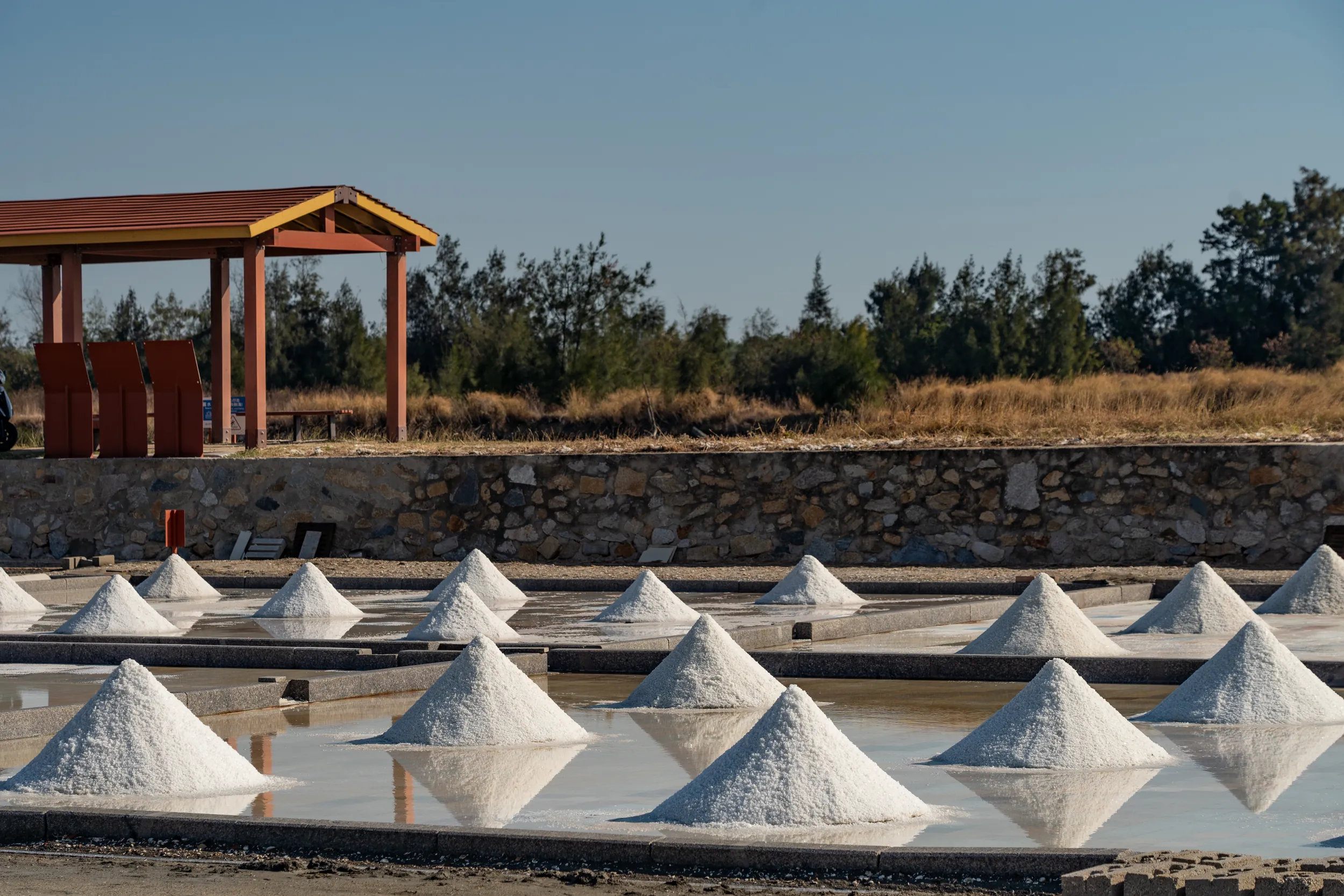 金門西園鹽場內的木造涼亭與結晶池，潔白的鹽堆清晰倒映在水面上，呈現金門東半島靜謐的鹽業文化風貌