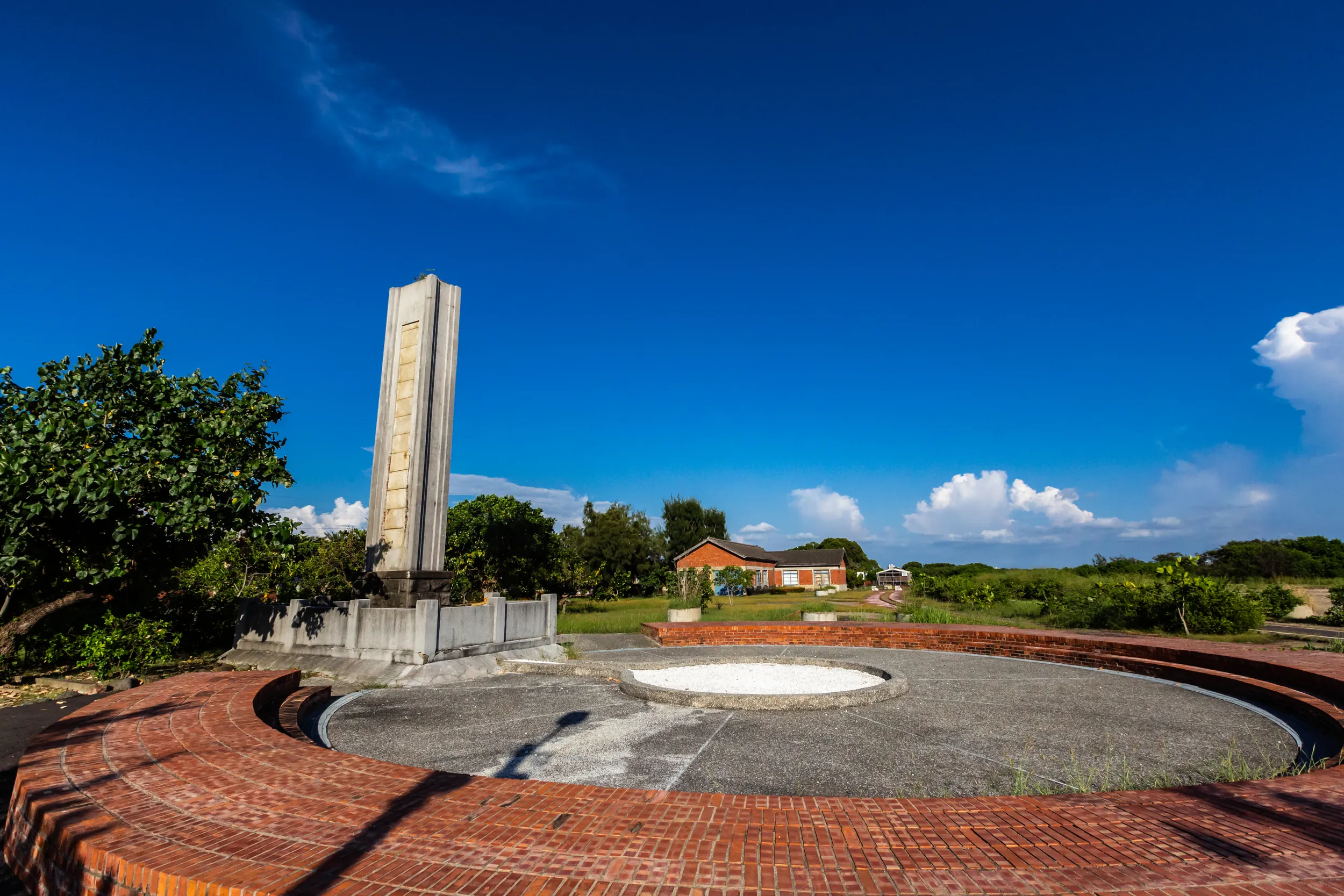 台南安順鹽場文化園區廣場上的高聳紀念碑地標，背景襯托著歷史紅磚建築與蔚藍天空，是遊客造訪台江國家公園的必拍景點。