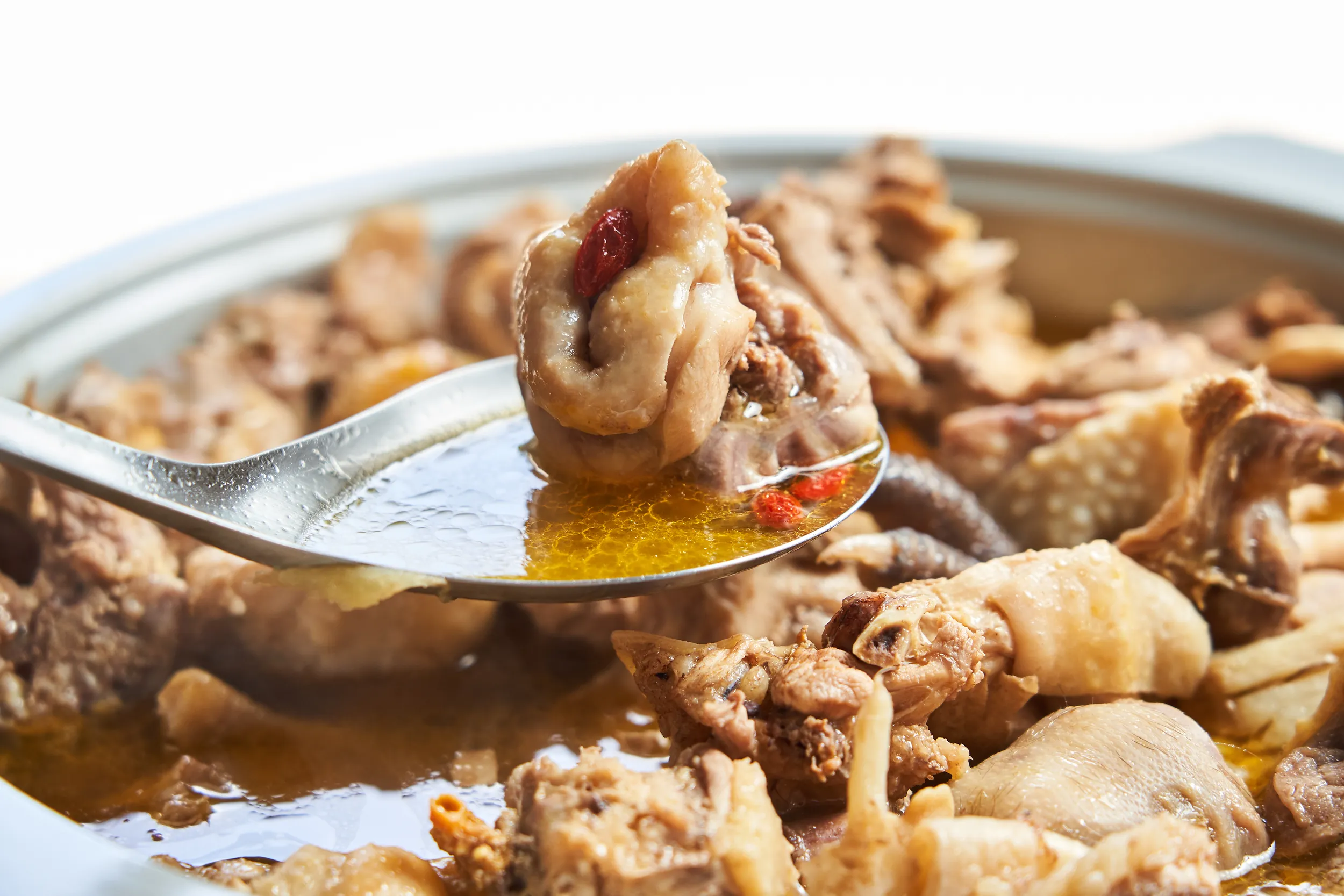 特寫鏡頭展示湯匙舀起台北知名的麻油雞鮮嫩肉塊，濃郁的金黃色湯頭中浮著麻油香氣與紅色枸杞，令人食指大動。