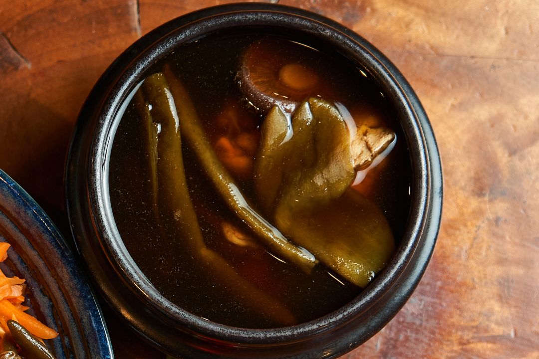 特寫一碗湯頭醇厚的剝皮辣椒雞湯，內含完整的綠色剝皮辣椒與鮮嫩雞肉，盛裝於日式陶碗中。