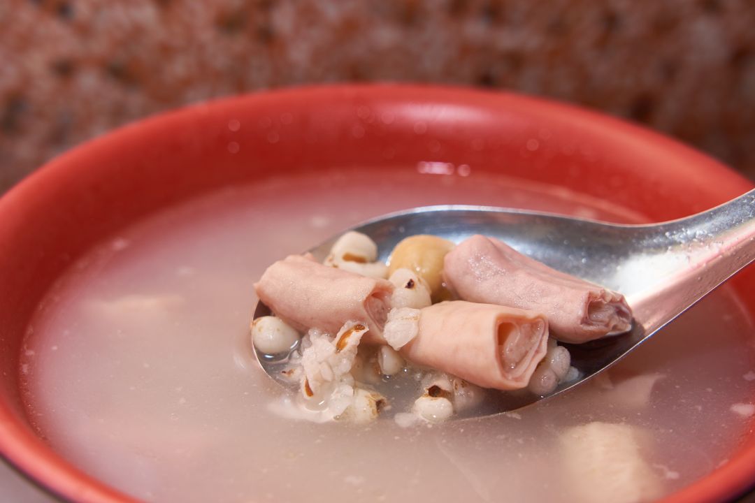 特寫鏡頭展示彰化在地的傳統四神湯,湯匙上舀滿了燉煮入味的軟嫩豬小腸與薏仁,湯頭濃郁呈現乳白色。