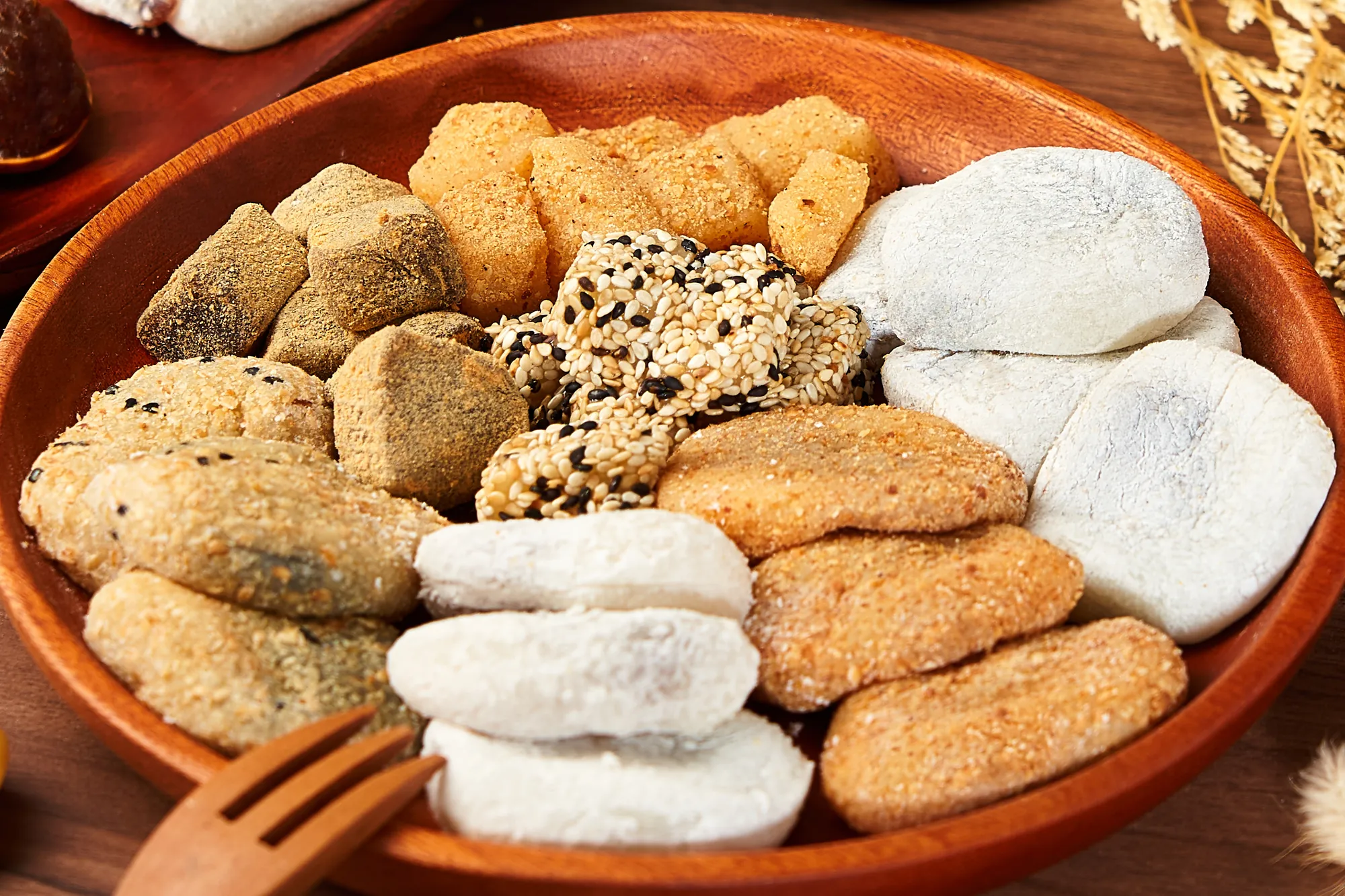 木盤上盛裝多種口味的傳統麻糬，包含裹滿花生粉、黑芝麻與原味糯米團，前方附有木製叉子，展示台式古早味甜點的豐富質感