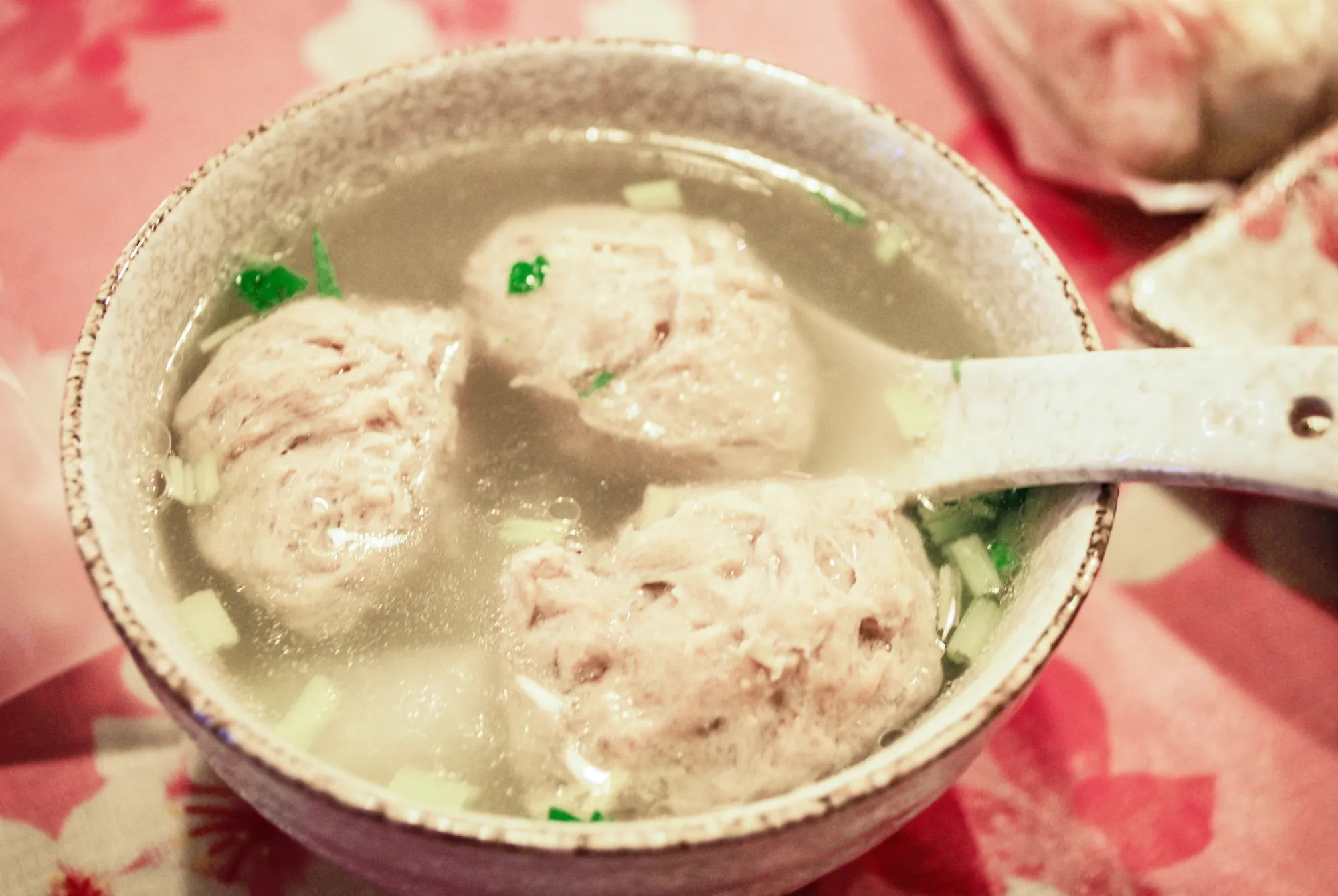 盛裝於陶瓷碗中的新竹貢丸湯特寫，三顆碩大飽滿的豬肉貢丸漂浮於清澈大骨高湯中，撒上芹菜末點綴，展示口感 Q 彈的台灣在地美食