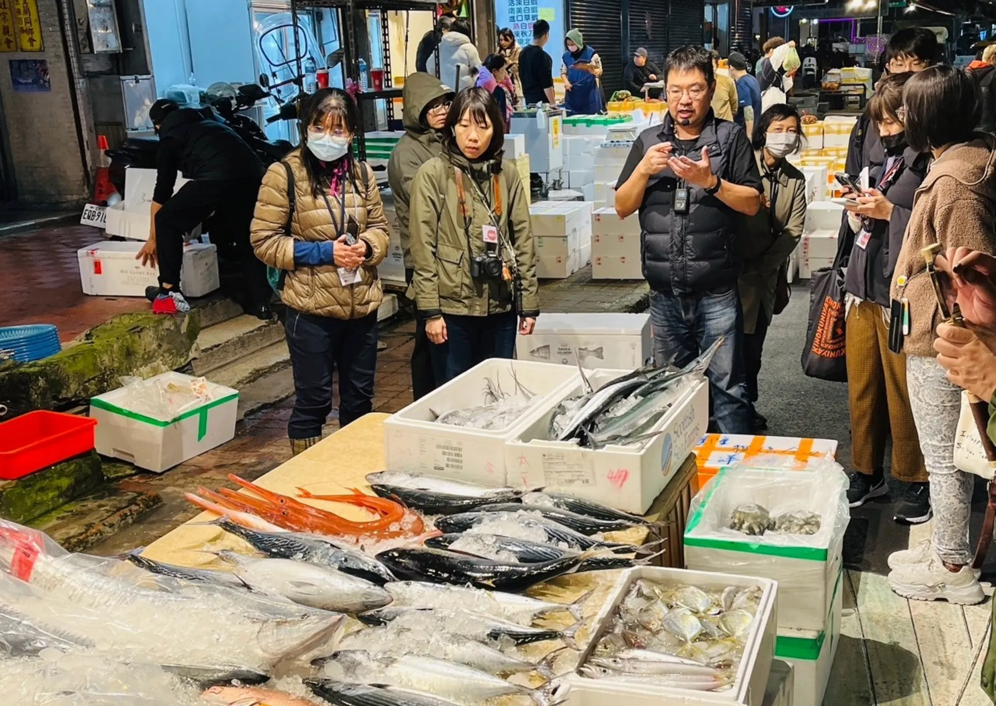 基隆見書店於深夜崁仔頂魚市舉辦文化導覽,講師正向遊客解說桌面上擺放的新鮮現捕魚獲