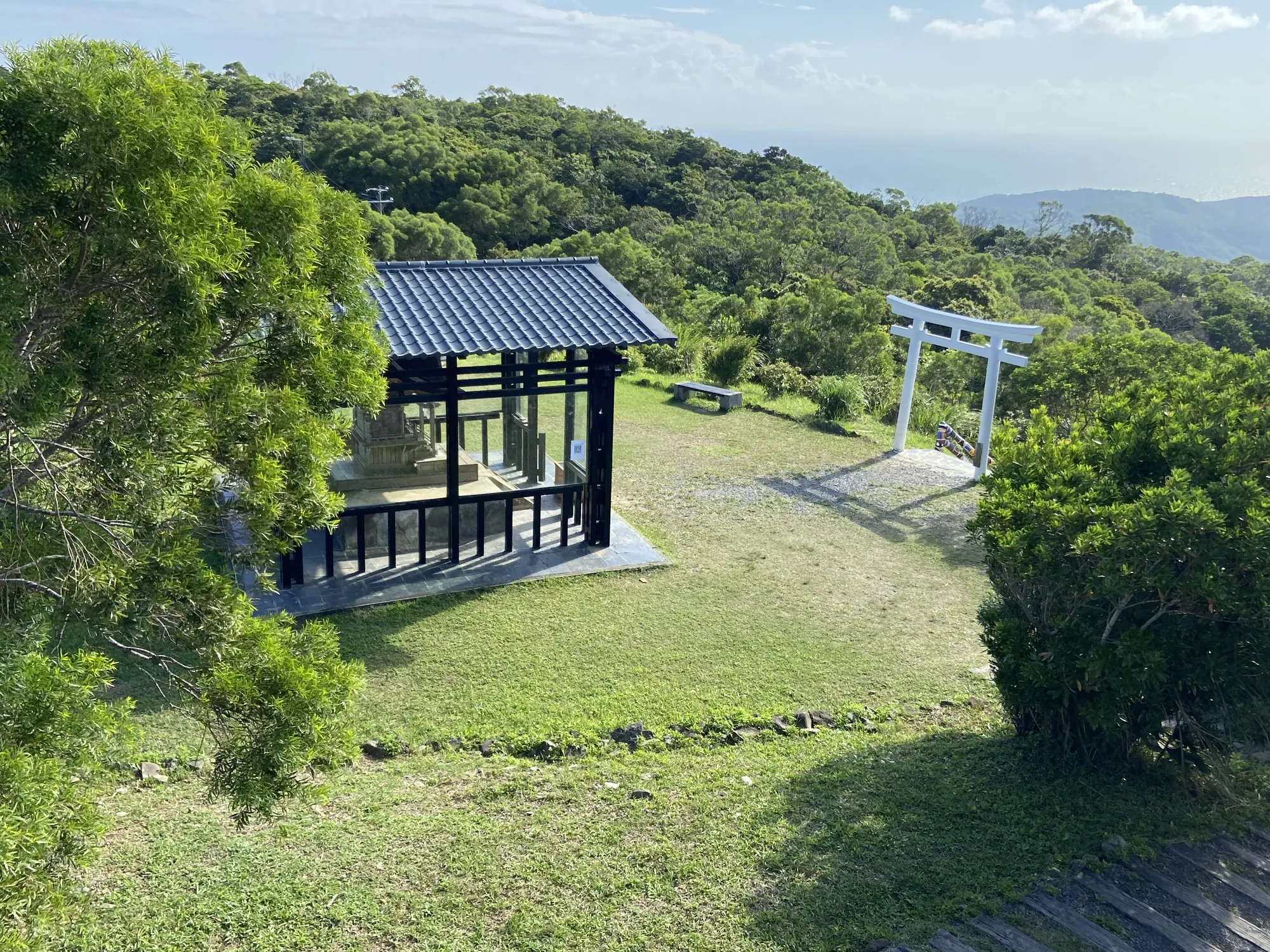 屏東牡丹高士神社遺址與純白鳥居，背景為山林與太平洋海景。展現高士佛部落遷至稜線後，與森林共生並發展段木香菇等林下經濟的歷史地景。