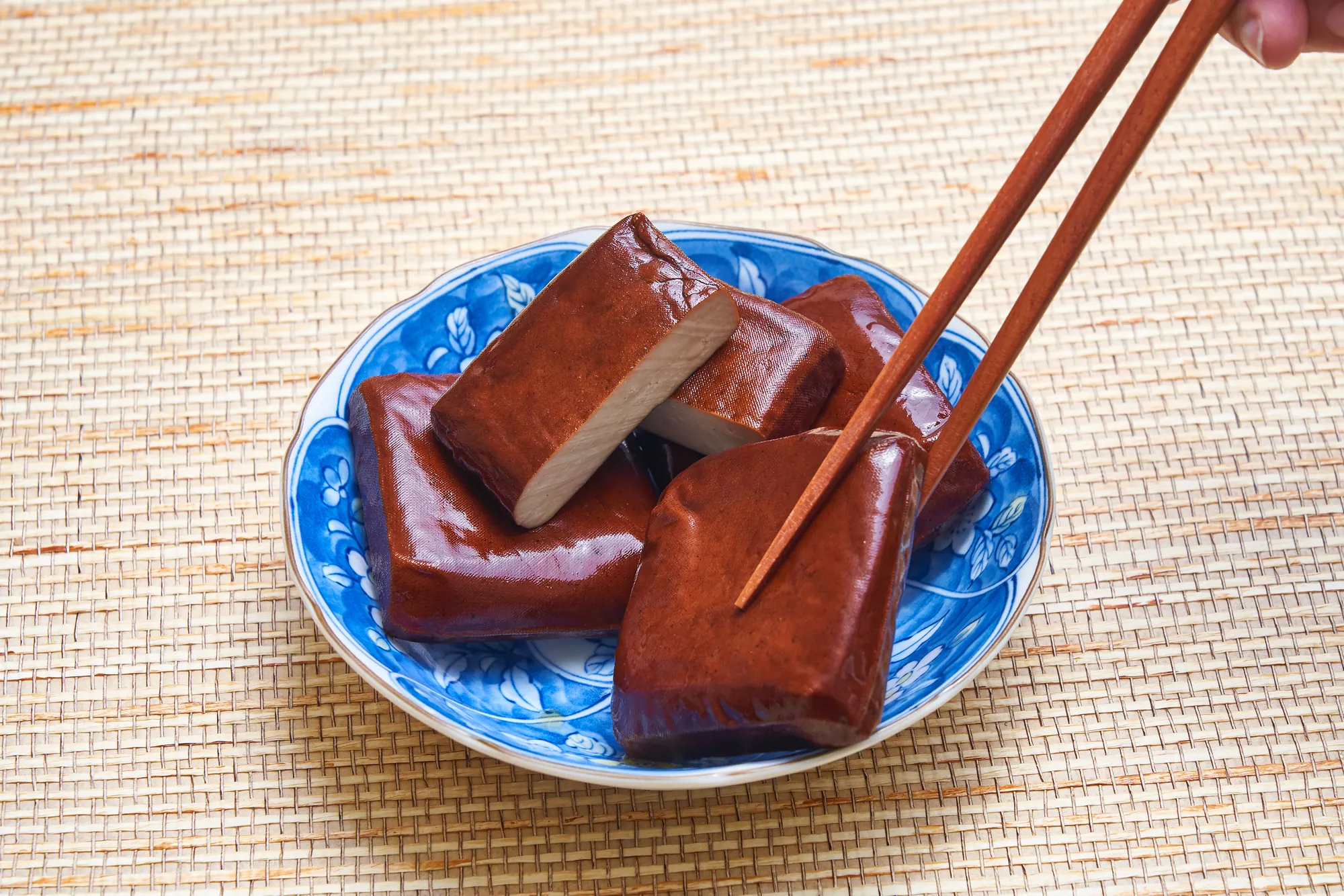 中式青花瓷盤盛裝的桃園大溪滷黑豆干，質地扎實色澤深潤，筷子夾起切開斷面。