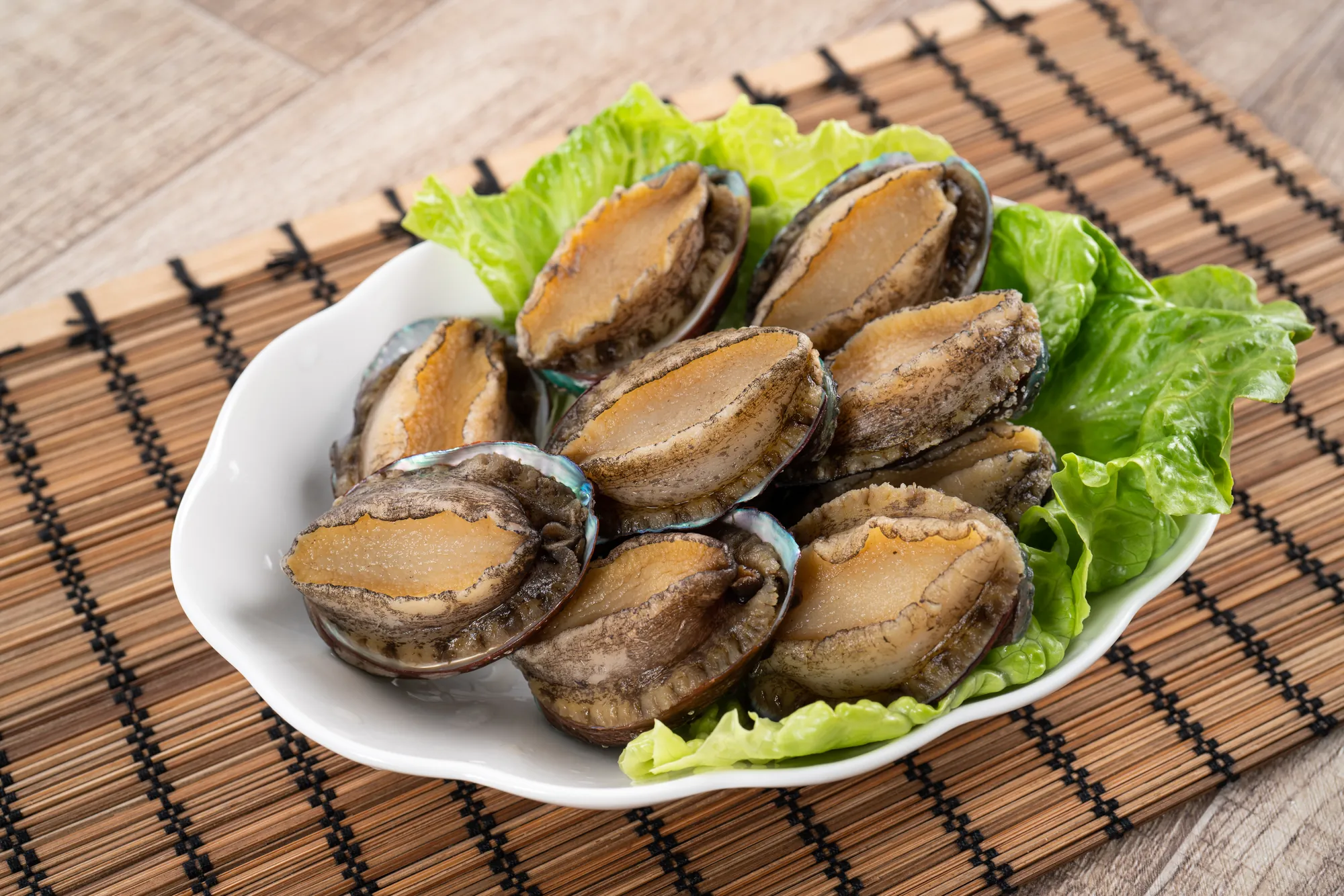 白盤盛裝的現撈九孔鮑魚，底部鋪墊新鮮生菜，展現台灣東北角特產海鮮的肉質飽滿質感。