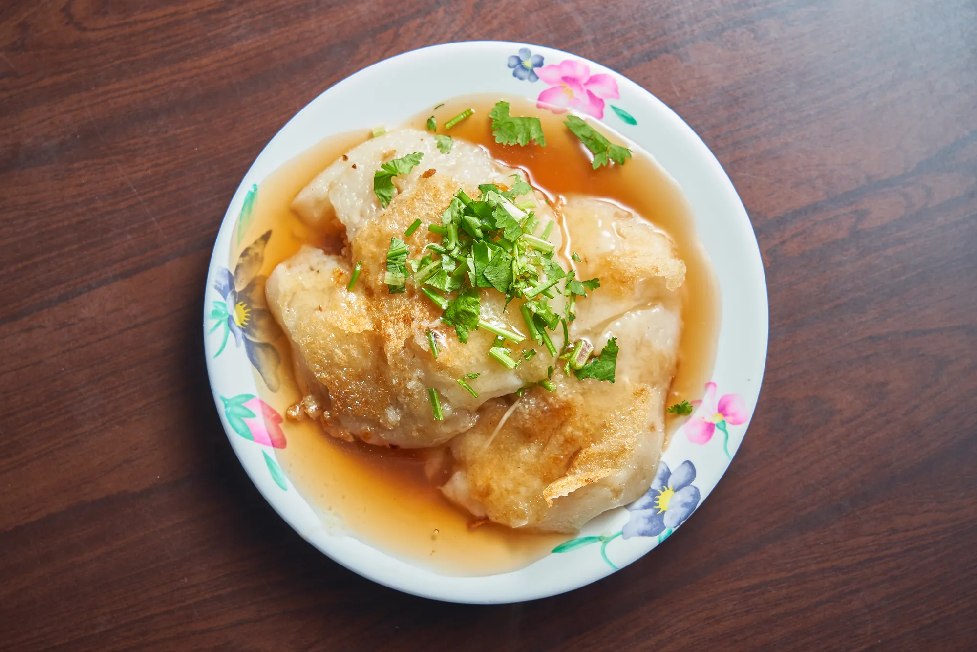 花紋盤子上的台南米粿，煎得金黃酥脆，上面淋上醬汁並撒了綠色香菜，呈現美味的台南在地小吃。