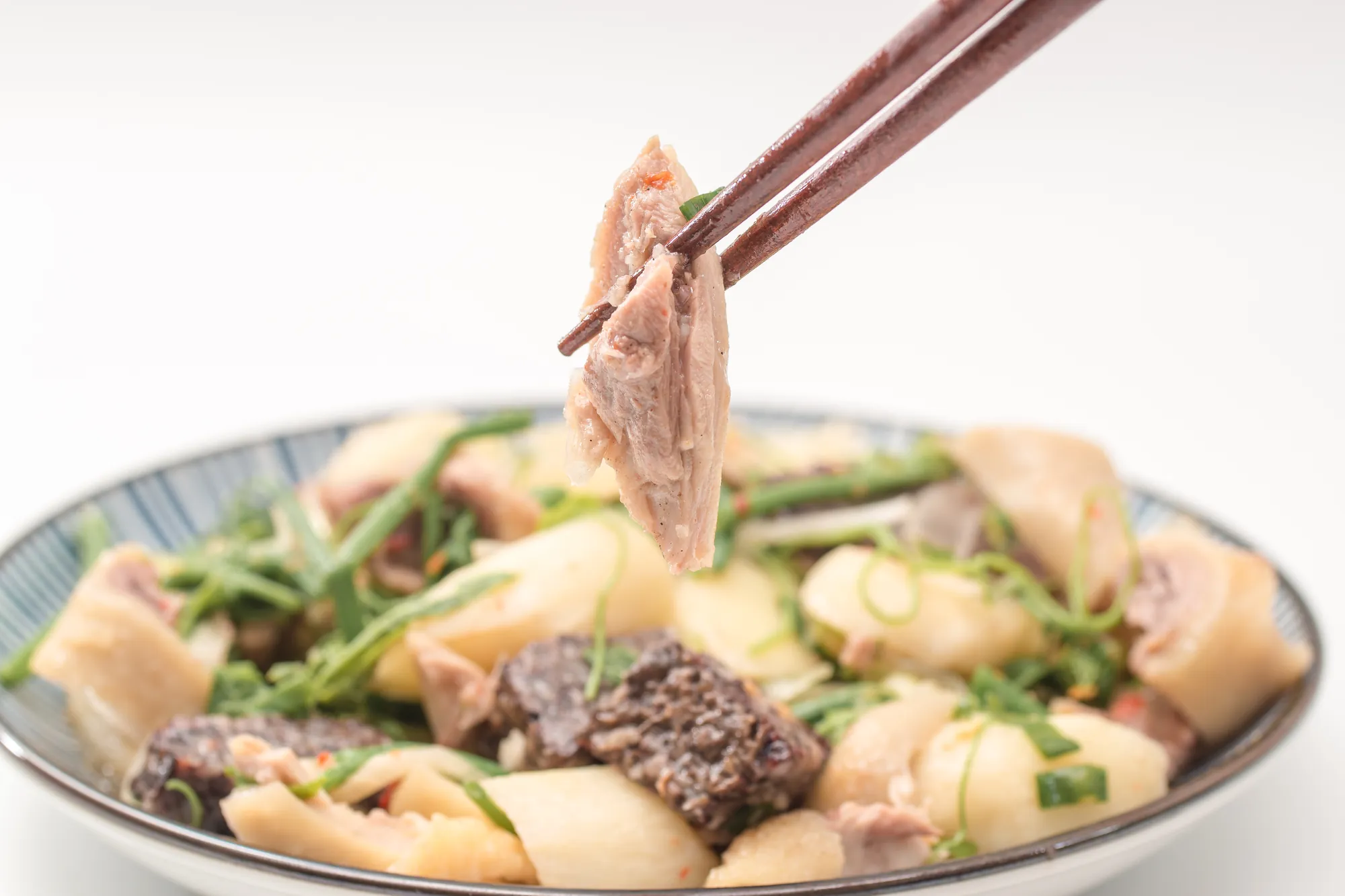 白色餐盒內的鹹水雞,包含去骨雞肉塊、切片苦瓜、百頁豆腐丁,並撒上切碎的蔥花、辣椒末與蒜頭,看起來調味辛辣開胃。