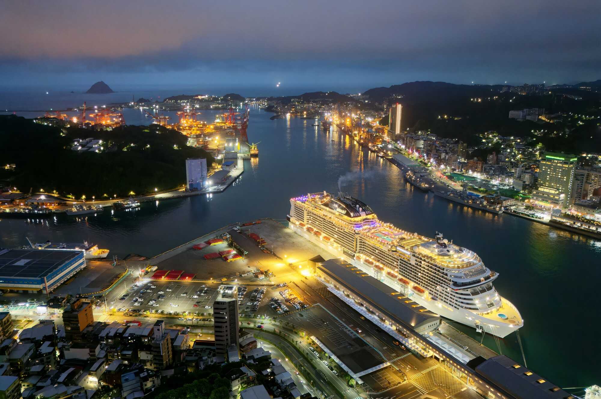 基隆港璀璨夜景空拍，大型豪華郵輪停泊於客運碼頭，背景為城市燈火與遠方的基隆嶼。