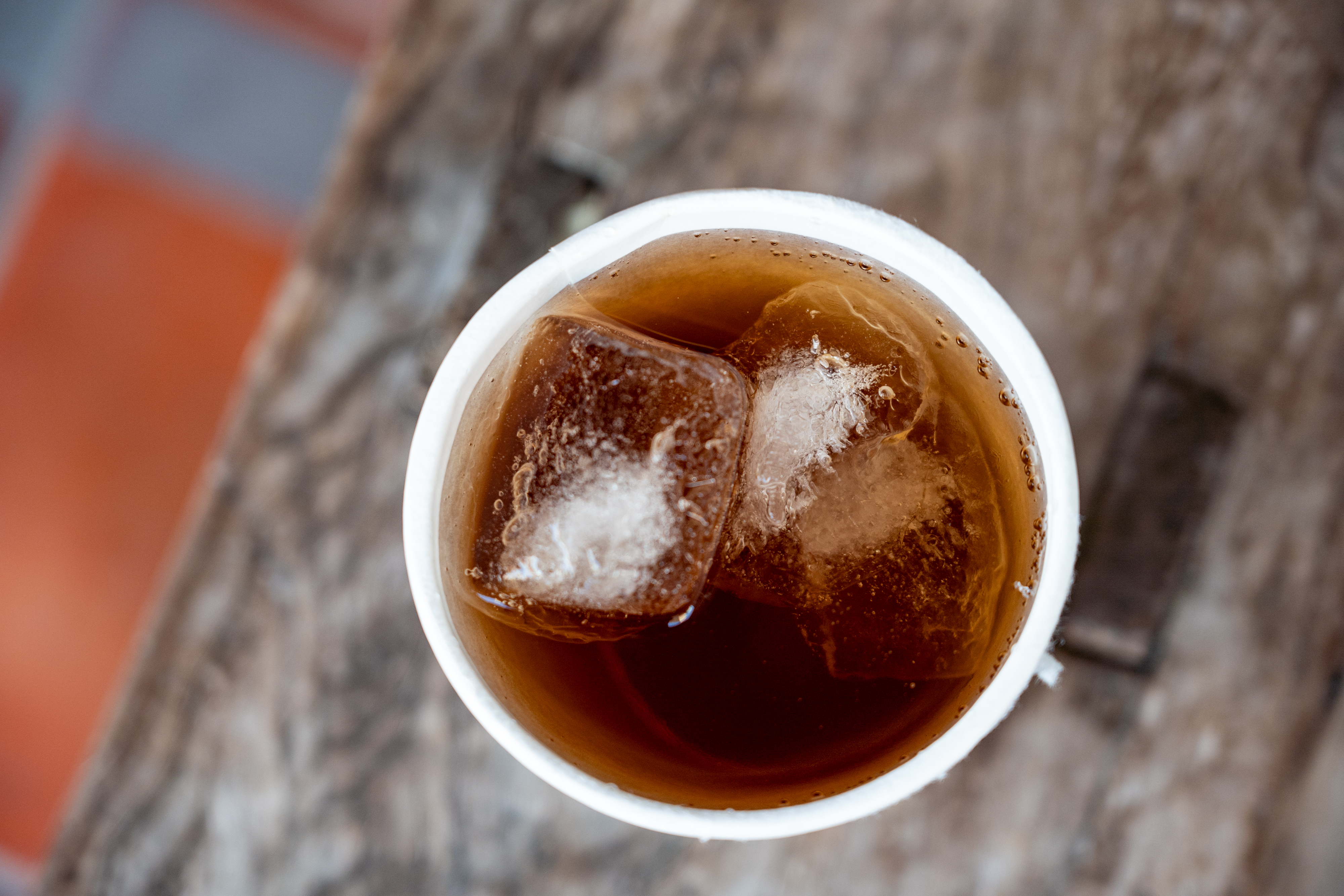 一杯盛裝在白色紙杯內的傳統台灣冬瓜茶，杯中漂浮著方形冰塊與檸檬片，背景為懷舊的橘紅色磚地板與長凳。