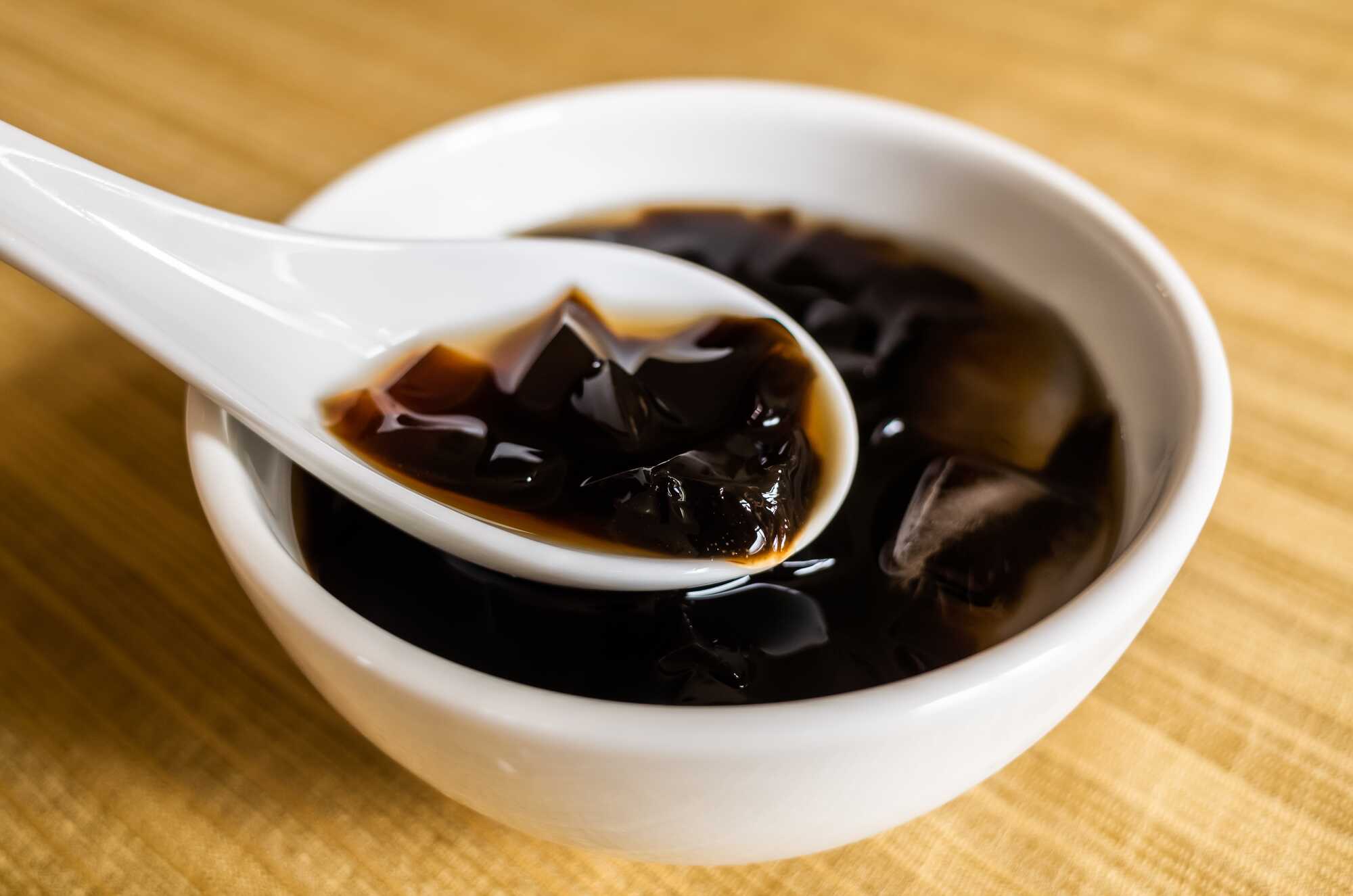 裝在白色陶瓷碗中的台灣傳統甜點仙草凍,白湯匙正舀起一塊晶瑩剔透的仙草。