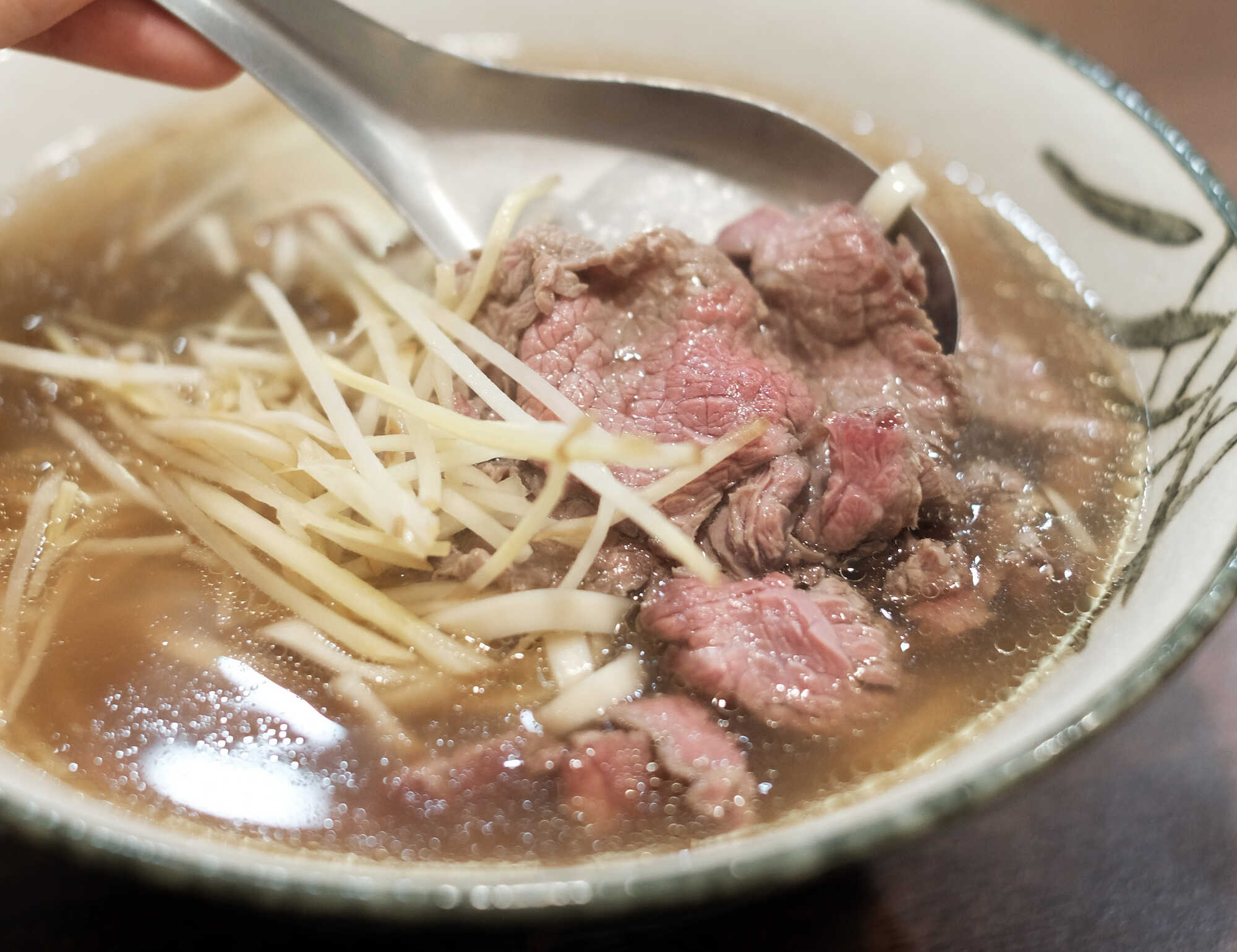 台南溫體牛肉湯特寫:湯匙撈起帶有粉嫩色澤的鮮牛肉與薑絲