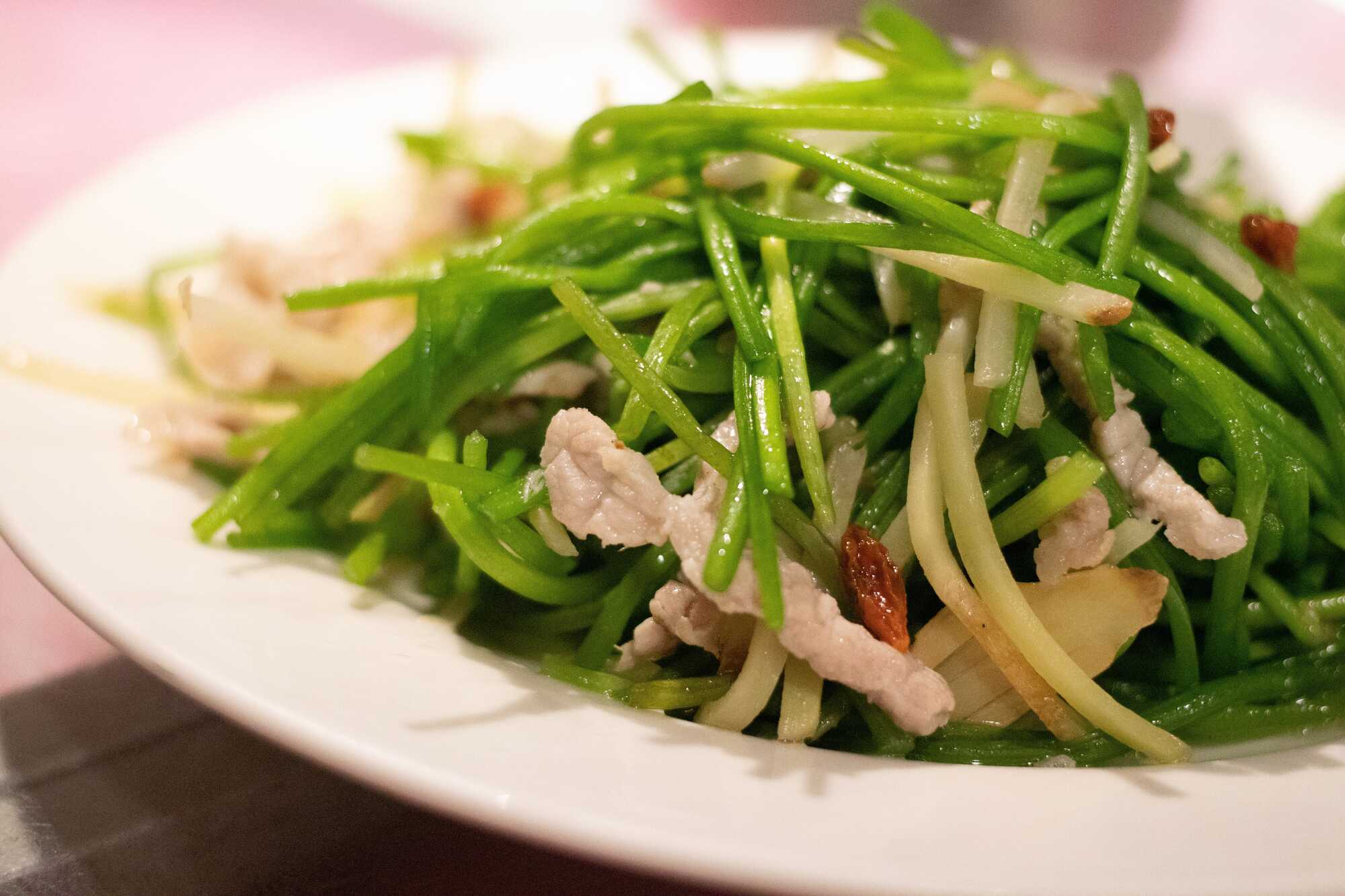 家常熱炒料理薑絲炒野蓮(水蓮),搭配肉絲與枸杞拌炒,盛裝於白盤中。