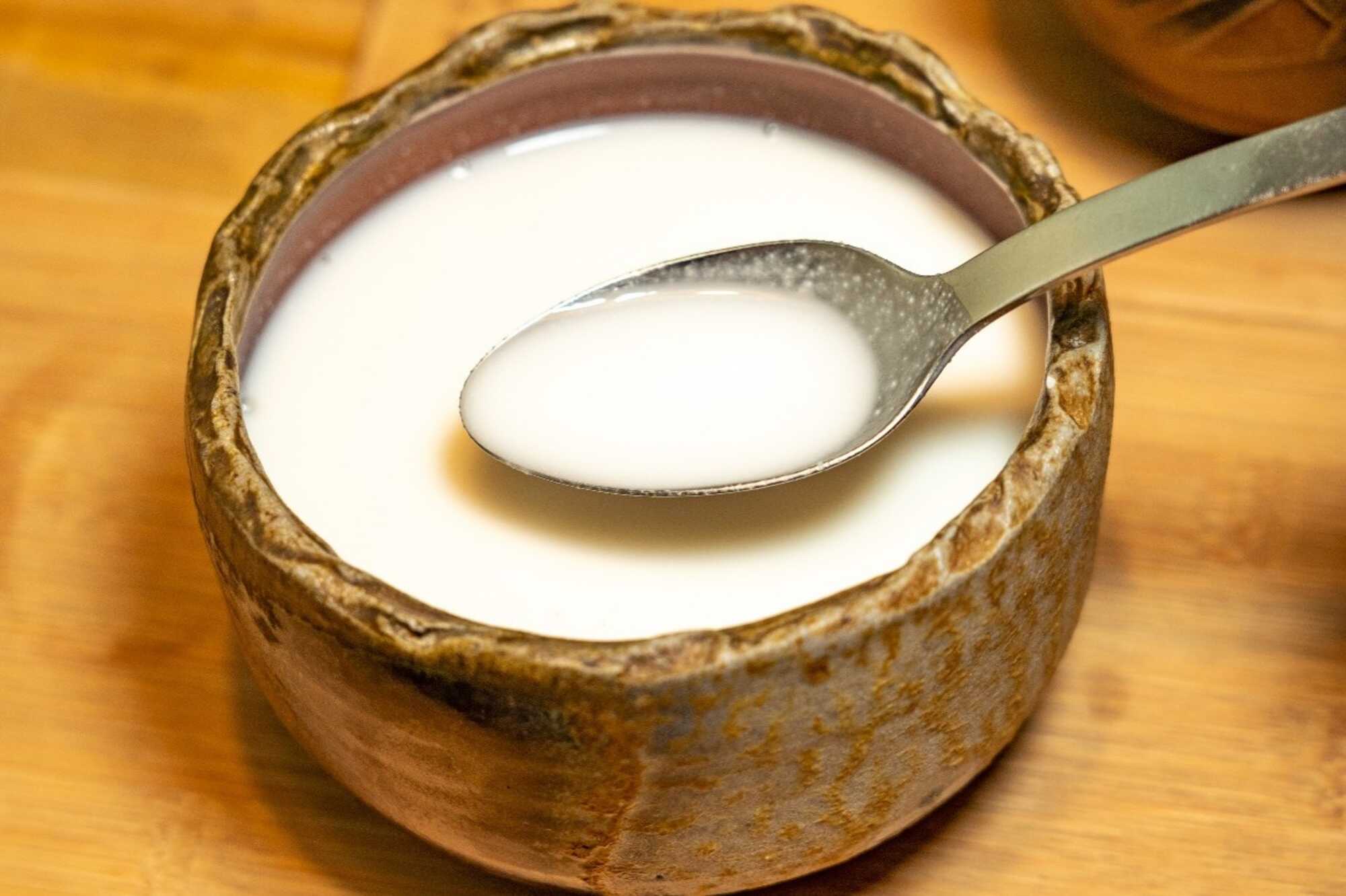 陶碗盛裝溫熱杏仁茶,湯匙舀起乳白色杏仁飲品。