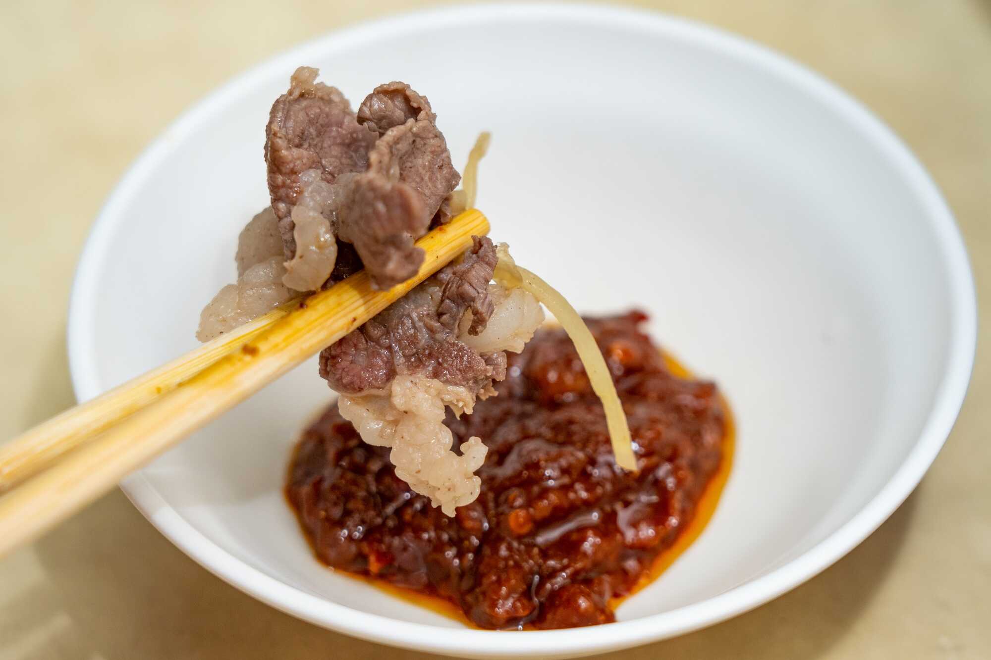 高雄岡山羊肉，切片羊肉搭配薑絲並蘸取豆瓣醬，呈現岡山傳統羊肉料理特色。