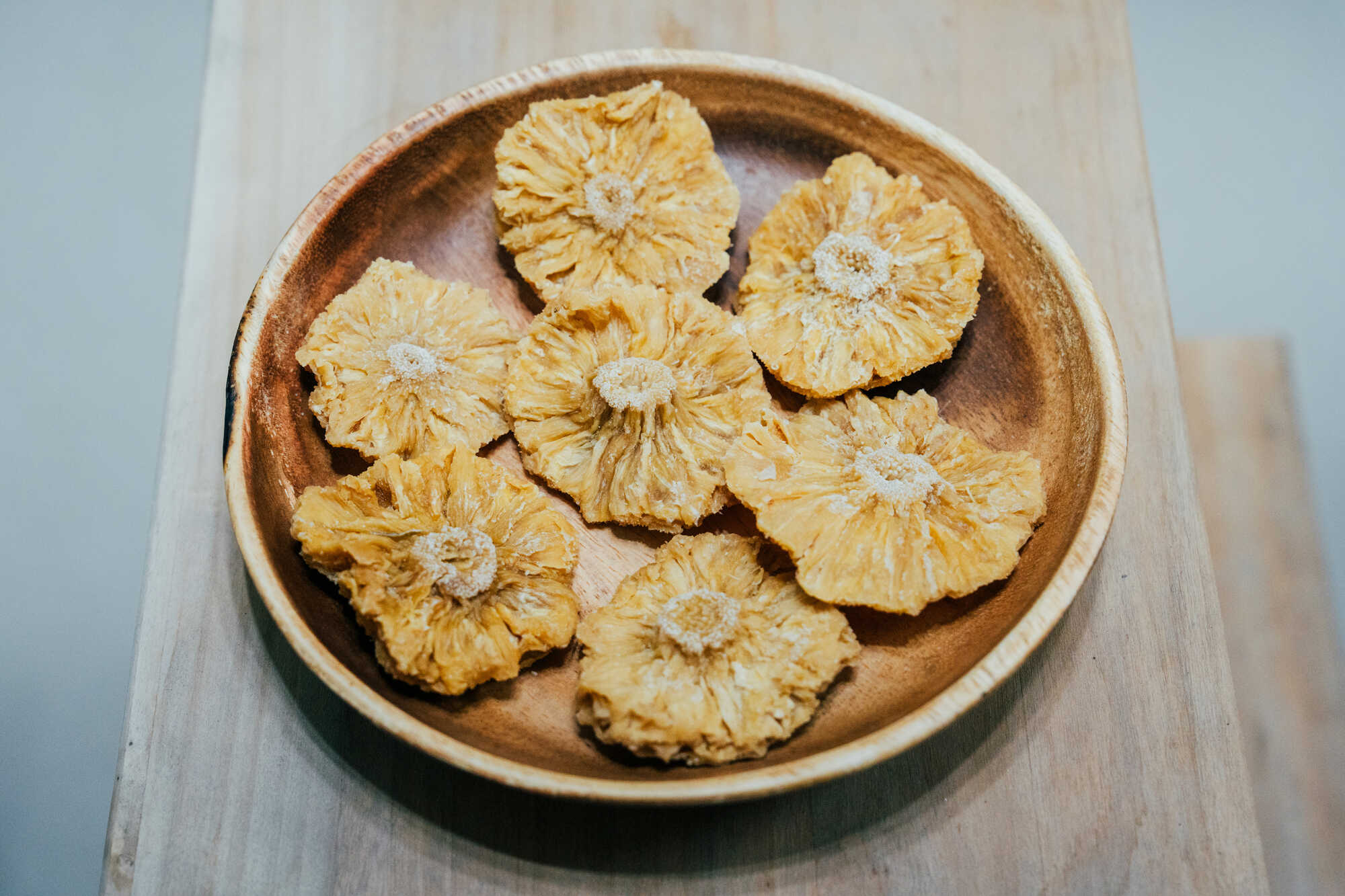 台南關廟鳳梨乾,金黃色圓形鳳梨切片呈現自然纖維紋理,整齊擺放在木製圓盤中。